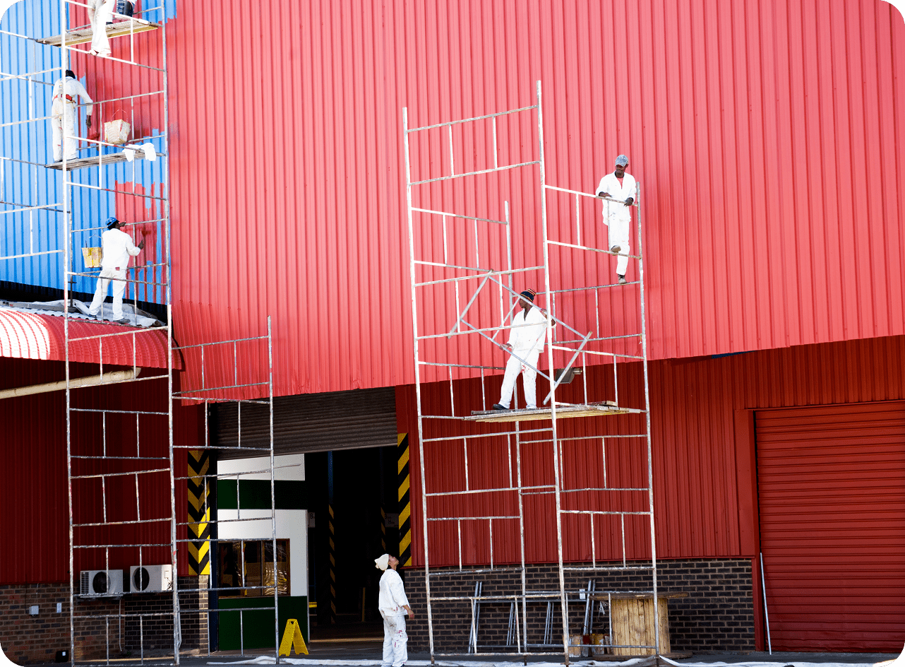 Workers painting a red warehouse exterior